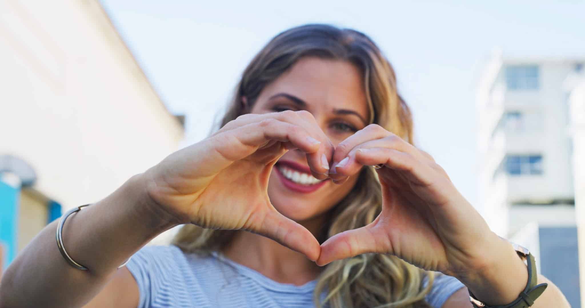 Hands, heart and smile of woman with sign of love, care and empathy in portrait in city, street or urban Australia. Compassion, emoji and face of model with happiness on holiday with support or style
