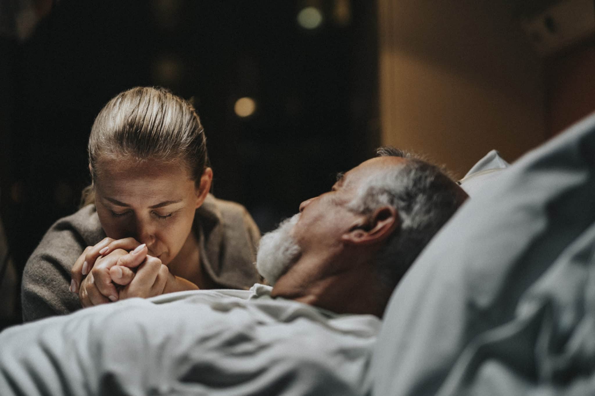 Daughter Kissing On Hand Of Father Lying Down In Hospital